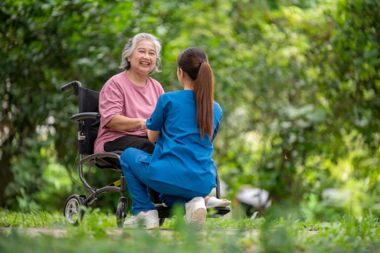 Elderly woman seated in a wheelchair with young caregiver or healthcare worker is standing behind re