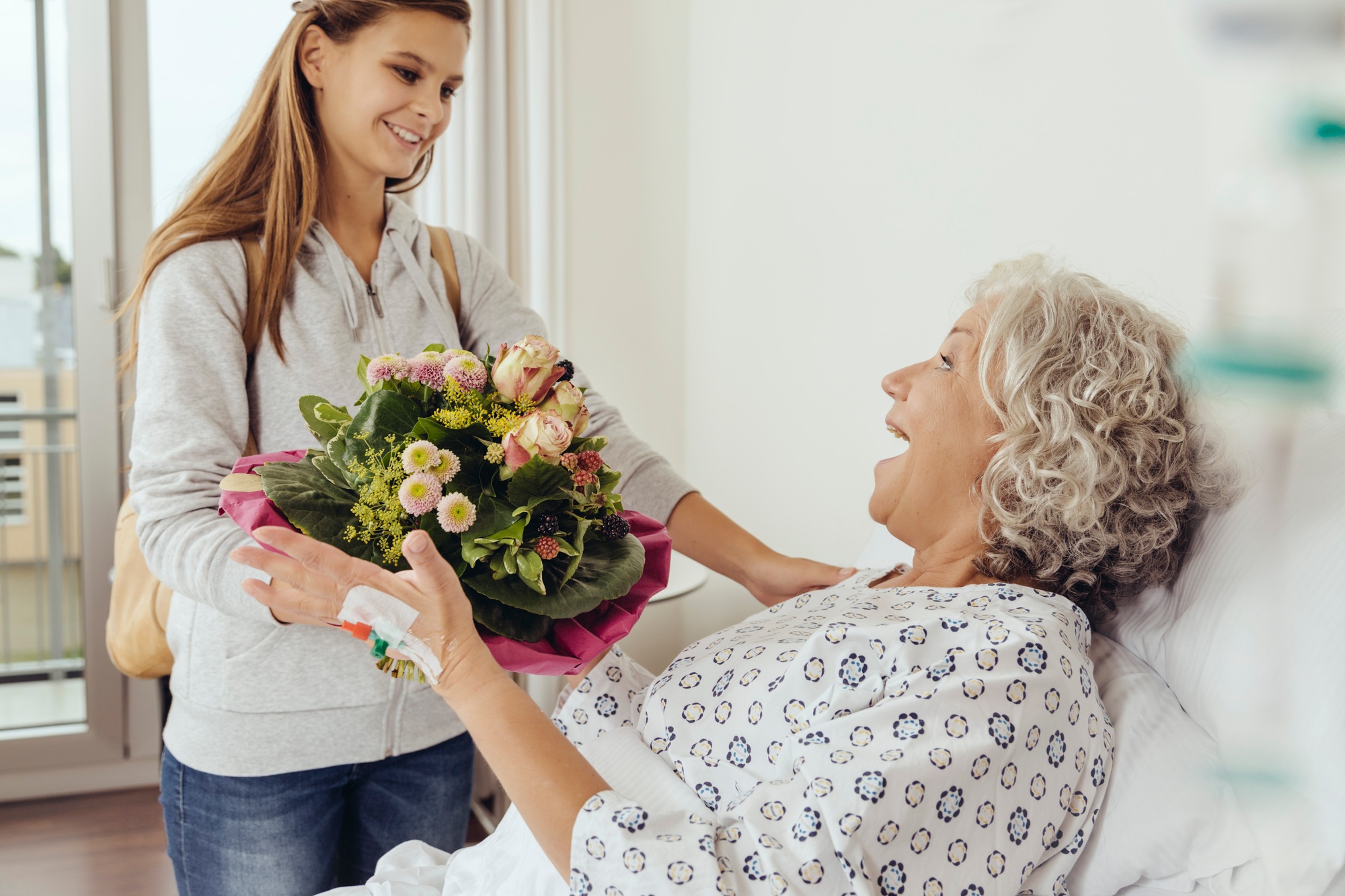 Granddaughter visiting grandmother in hospital, bringing bunch of flowers