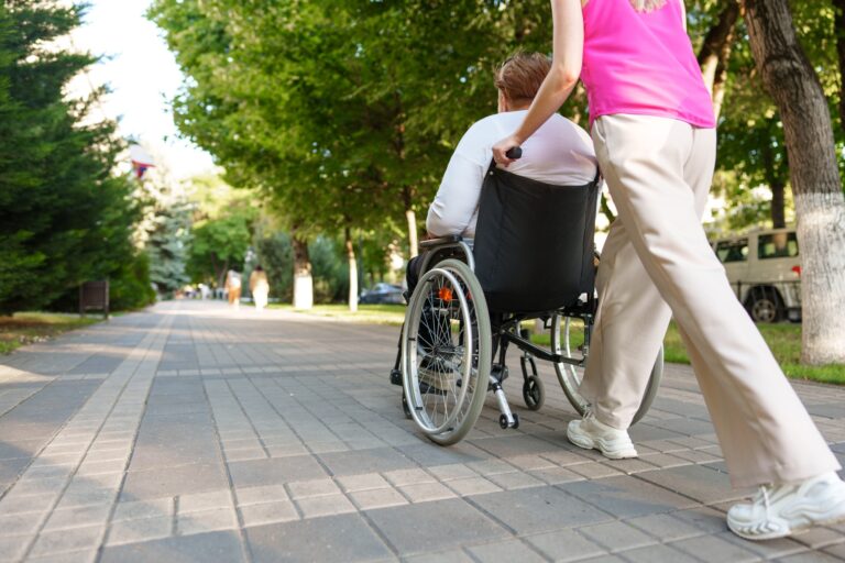 Young female caregiver pushing wheelchair with female person with disability across city street